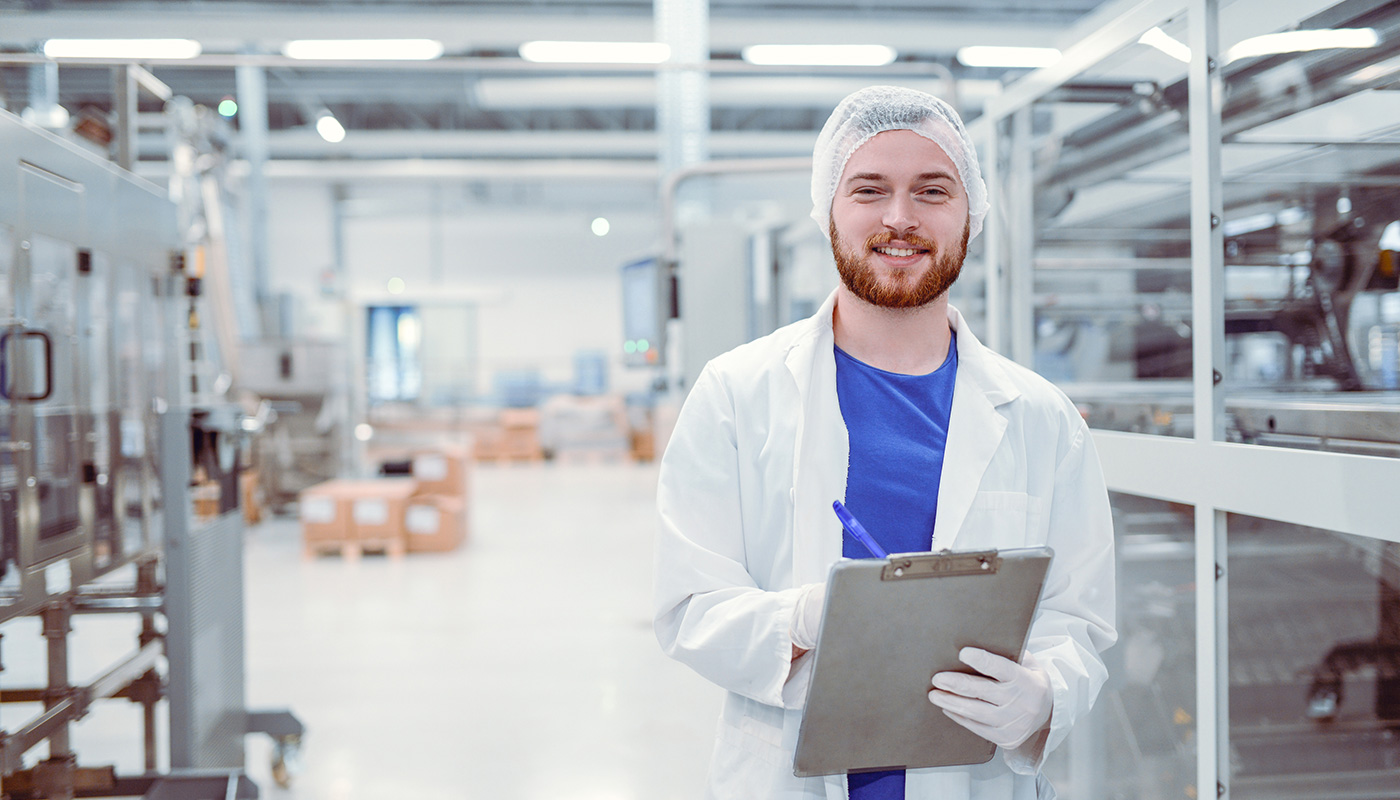 A young smiling man holding a clipboard in a cleanroom